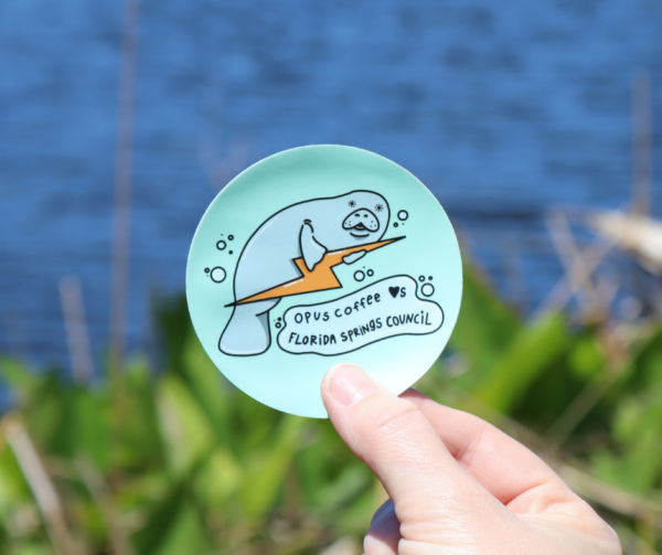 Sticker of a manatee holding a lightning bolt with the words "Opus Coffee Loves the Florida Springs"