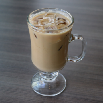 Iced cortado in a clear mug with handle on a brown table. 