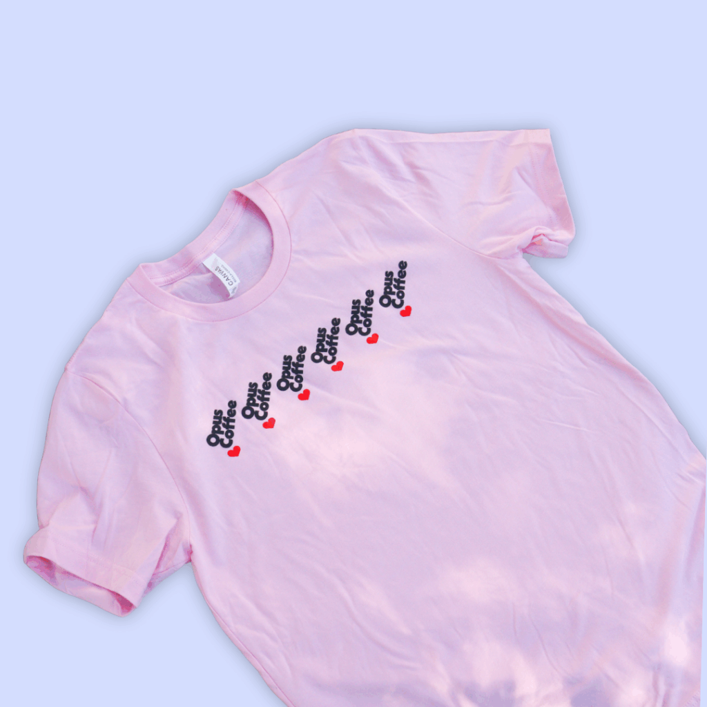 pink T-shirt with opus heart drip repeating logo. on light lavender background.