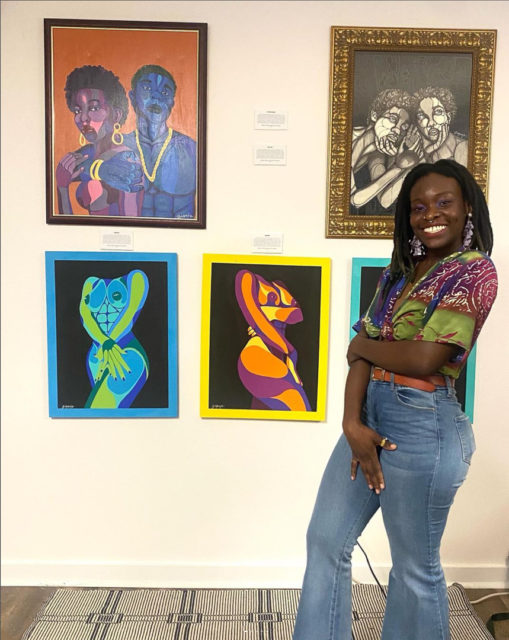 Woman standing smiling in front of her art pieces at an art show