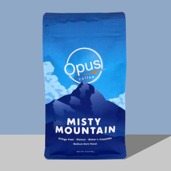 Opus Coffee Misty Mountain Blend coffee bag on a blue background. The coffee bag features a dark blue mountain with a blue sky and clouds and in white writing it says "Misty Mountain."